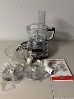 Full view of KitchenAid food processor with base, work bowl, lid, multiple blades and accessories, instruction manual, some accessories in original packaging