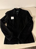 Full front view of the black suede ladies jacket laid flat, showing form and shape with zipper closure visible