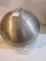 Spherical silver light fixture showing perforated metal surface with hanging attachment and intact Artemano label