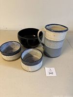 View of all four pottery items together: pitcher, black bowl, two blue and white smaller bowls.