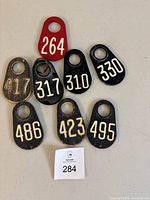 Eight vintage livestock ear tags in black and red with white numbering, some showing surface wear and scratches.