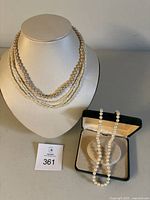 Photo of three pearl necklaces arranged on a white display bust and a green box containing another necklace.