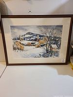 Framed watercolor painting of a winter landscape featuring buildings, trees, and hills under a cloudy sky.