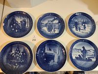 Photo showing six of the cobalt blue Royal Copenhagen Christmas plates with winter and Christmas scenes in blue and white, arranged on a table.