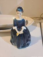 Close-up photo of the Royal Doulton Cherie figurine in dark blue dress holding a yellow item, showing detailed facial features and glossy finish.