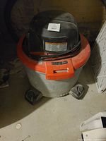 Shop Vac unit photographed from above showing orange top, black motor cover, coiled hose, and wheels on bottom.