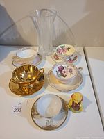 Photo showing three tea cups with saucers, a crystal vase, and Winnie the Pooh figurine arranged on a table.