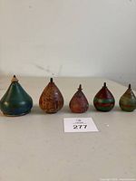 Five vintage wooden spinning tops in a row, varying in size and color including green, natural wood, and painted stripes, each with metal tips.