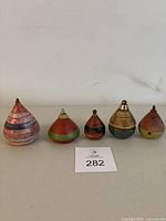 Front view showing five vintage wooden spinning tops in various sizes and colors with metal tips on a table