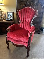 Full view of red upholstered Victorian-style parlor chair with carved wooden frame in room