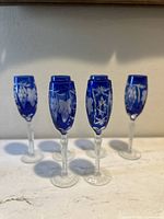 Five cobalt blue crystal wine flutes with clear stems displayed together showing etching details