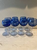 Front view of eight cobalt blue cut crystal goblets with grape and leaf designs on a white surface.