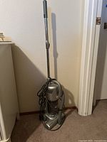Full view of gray upright stick vacuum cleaner with hose attachment and power cord coiled.