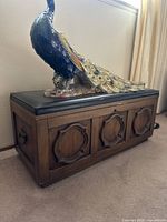 Full side view of the wooden chest showing the design and padded top with a decorative peacock figure on top.