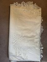 Folded large vintage lace tablecloth showing the overall fabric and lace design details.