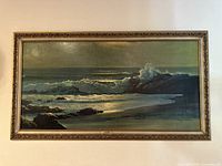 Front view of framed seascape painting showing waves, rocks and ornate frame