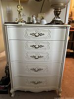 Front view of the white French Provincial style dresser with five drawers featuring carved details and brass handles