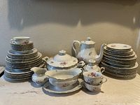 Full view of vintage bone china tea set with teapot, creamer, sugar bowl, covered serving bowl, gravy boat, stacked plates, and teacups with floral and gold trim design.