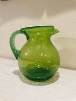 Side view of the green hand blown bubble glass pitcher showing rounded body, spout, and handle.