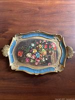 Full view of the vintage Florentine tray showing the floral painting and blue and gold ornate border with handles.