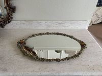 Top-down view of the oval vanity tray showing the mirrored surface and ornate gold filigree edge with amber stones at each short end.