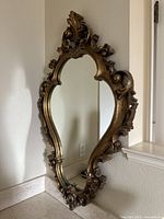 Full view of the ornate vintage wall mirror leaning against a wall, showing the shape and frame.