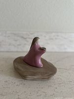 Side view of the ceramic figurine showing the hair texture and bowl in hand on wood base