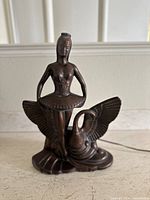 Front view of a brown-toned ballerina and swan figure showing detailed tutu, corset, and crown on ballerina with wings of swan spread widely behind her.