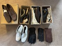 Top-down image of five pairs of men’s shoes and three pairs of gloves arranged on carpet, shoes mostly black and brown with one white pair, gloves black and brown leather