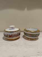 Photo showing two porcelain pieces side by side on a marble surface, a covered jar and an ashtray.