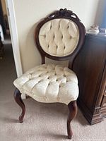 Full view of the vintage Victorian chair showing cream tufted fabric seat and backrest with carved wooden frame and curved legs.