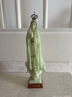 Front view of a glow-in-the-dark Virgin Mary Fatima figurine showing the praying figure with crown and rosary, standing on a wooden base.