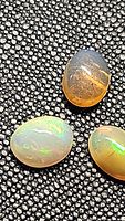 Three natural Ethiopian opal cabochons on textured black background showing multicolored play-of-color and translucency.