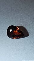 Close-up photo of a pear-shaped deep orange spessartite garnet gemstone with facets visible and a glossy finish.