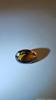 Side angle view of a deep cognac colored oval cut Madeira citrine gemstone on white background with shadow.