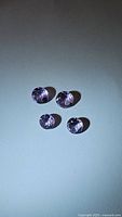 Four round cut natural amethyst gemstones with a pink-purple hue, 6mm approx. viewed at an angle showing faceting and color.