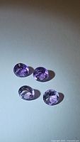 Four round cut natural amethyst gemstones placed on white surface.