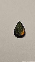 Pear-shaped bi-colored sapphire showing green and orange colors on a plain surface.
