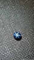 Close-up of natural blue star sapphire cabochon showing six-ray star reflection on textured black surface