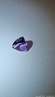 Photo showing deep purple trillion cut amethyst gemstone on white surface with light reflections.
