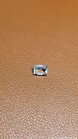 Photo showing the rectangular emerald cut aquamarine gemstone on a textured brown background with natural light highlighting its clarity and blue hue.