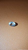 Photo of natural oval cut aquamarine gemstone placed on textured brown surface under light showing its color and clarity.