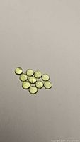 Thirteen round cabochon peridot gemstones laid out on a flat surface showing their uniform size and apple green color.