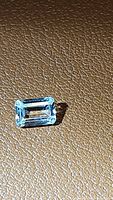Close up of the natural untreated emerald cut light pastel yellow sapphire gemstone on a textured brown surface