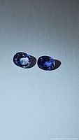 Two oval cut natural blue sapphires from Ceylon displayed on a flat surface with lighting highlighting their blue color and cut.
