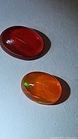 Two natural oval cabochon fire opals with red and orange coloring, showing multicolored play of color.