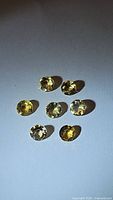 Seven round cut natural golden citrine gemstones arranged on white background under lighting showing facets and color.