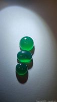 Three natural green onyx cabochon gemstones arranged vertically on a white background with spotlight illumination