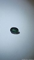 Oval natural blue green sapphire gemstone placed on white background, showing color and cut.