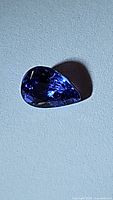 Close-up photo of pear-shaped tanzanite gemstone with dark blue and violet hues, showing facets and cut.